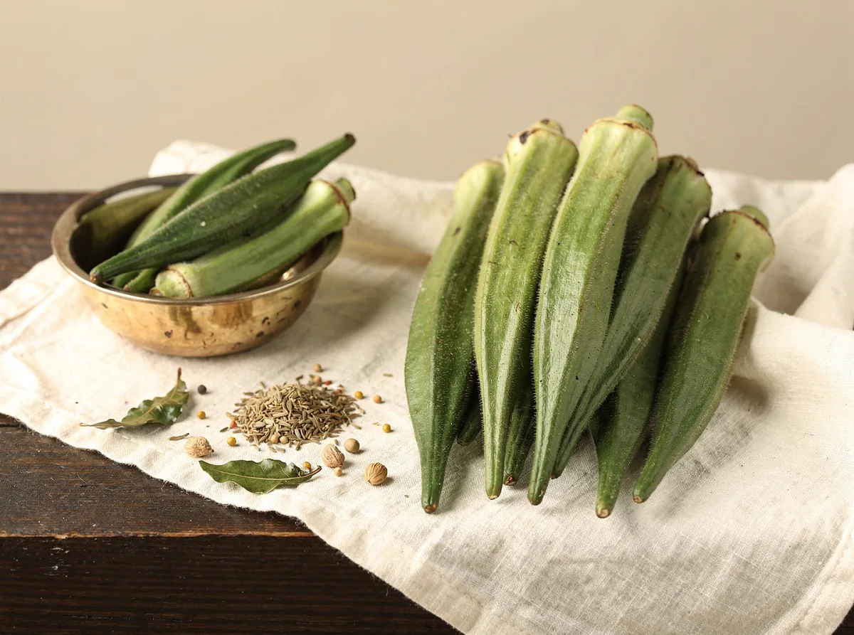 Fresh green okra pods with ridged texture, whole and uncut, on a light background.